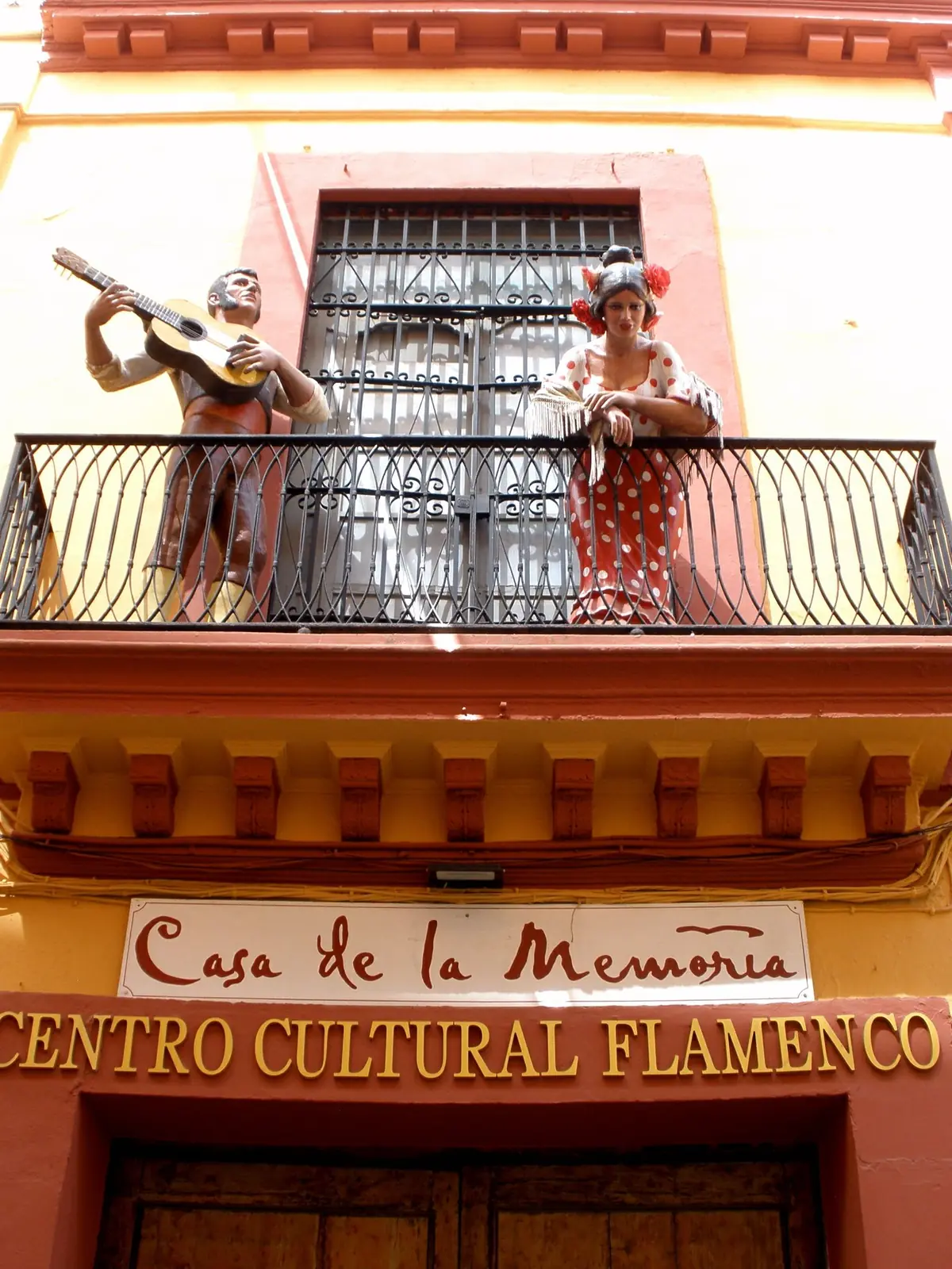 The ochre and red facade of Casa de la Memoria on Calle Cuna, with a painted guitarist and dancer on the balcony and the centre's name on a sign below