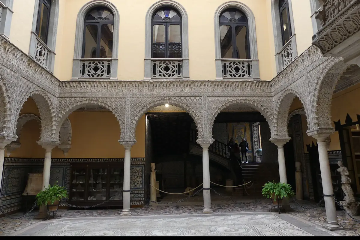 The ornate plaster arches and yellow walls of a Seville palace patio with a mosaic floor