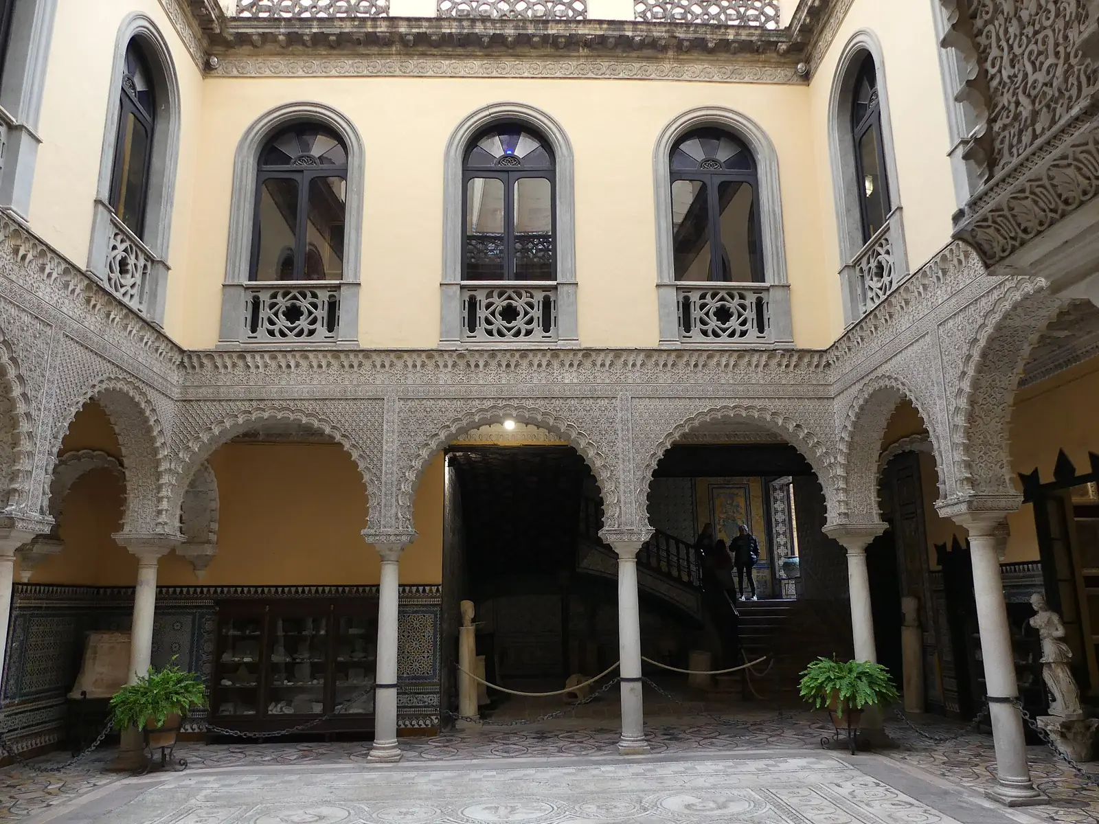 The carved plaster arches and yellow walls around the mosaic-floored patio of the Palace of the Countess of Lebrija in Seville
